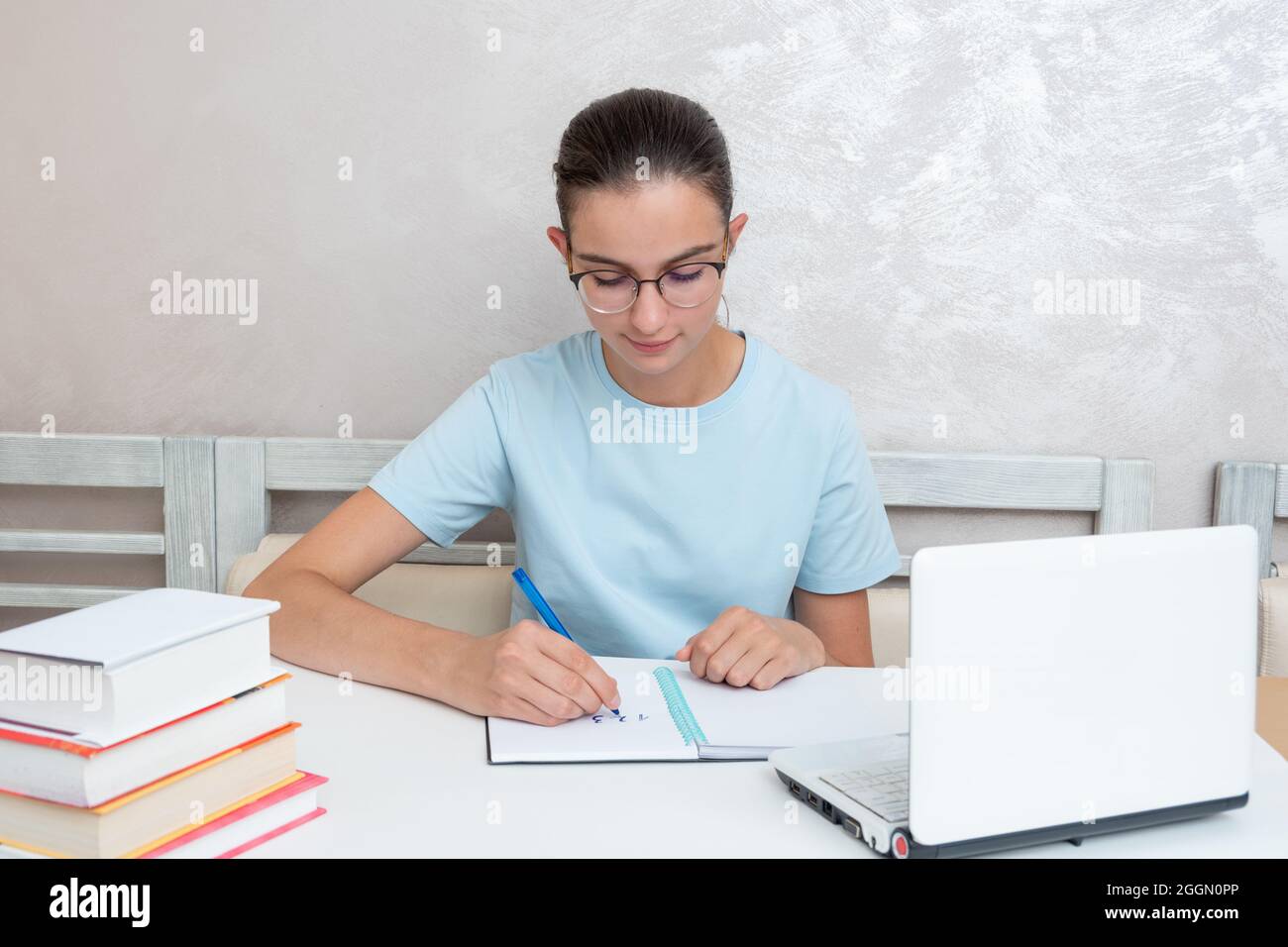 A smiling girl student sitting at a table with a laptop writes a task ...