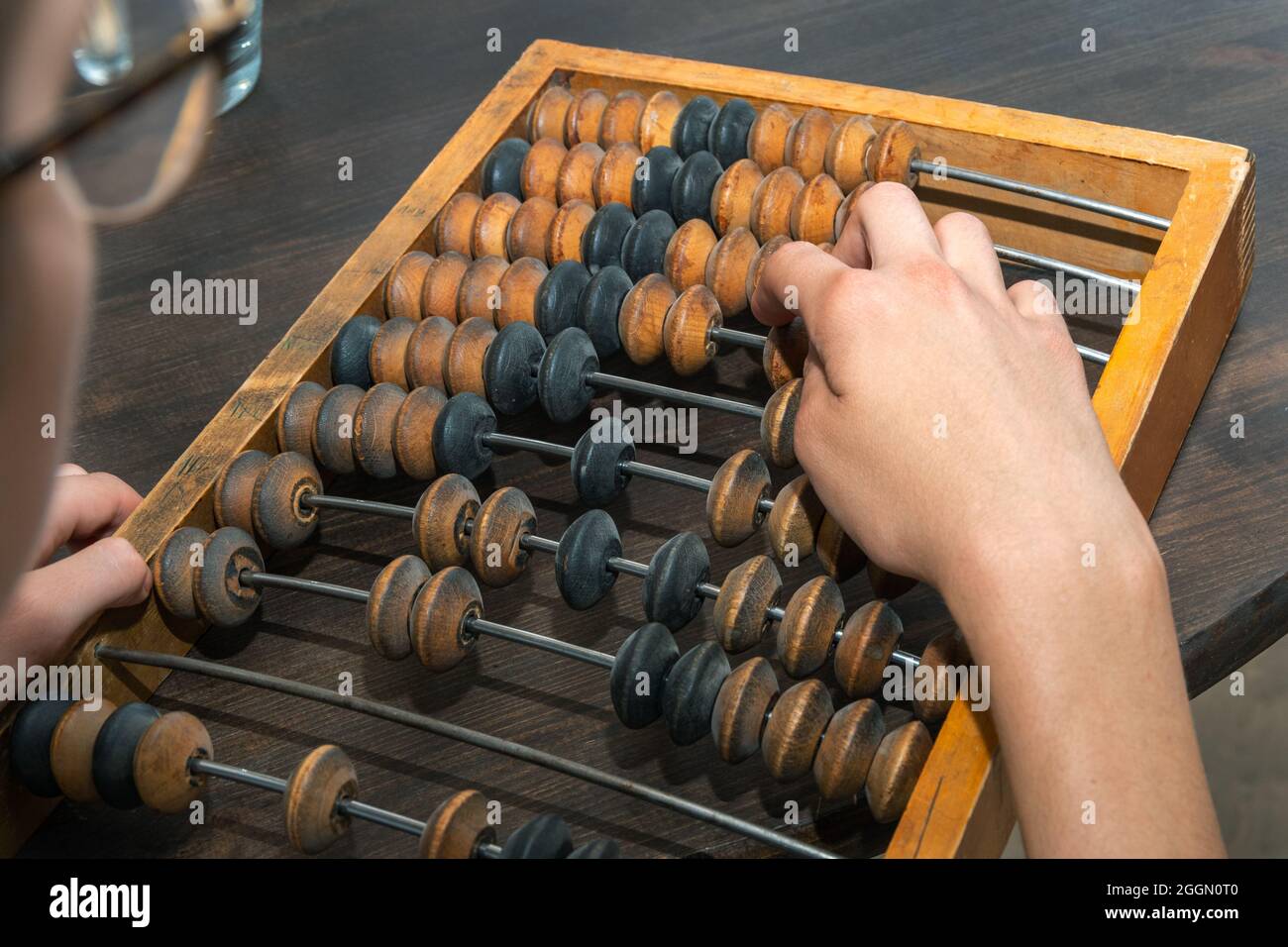 Female hand counting on ancient retro old abacus, moving beads on a wooden background, close-up. Business and financial concept. Saving money. Calcula Stock Photo
