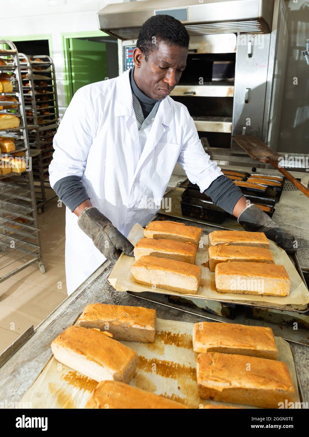 Africanamerican baker spreads freshly baked bread on a pallet Stock
