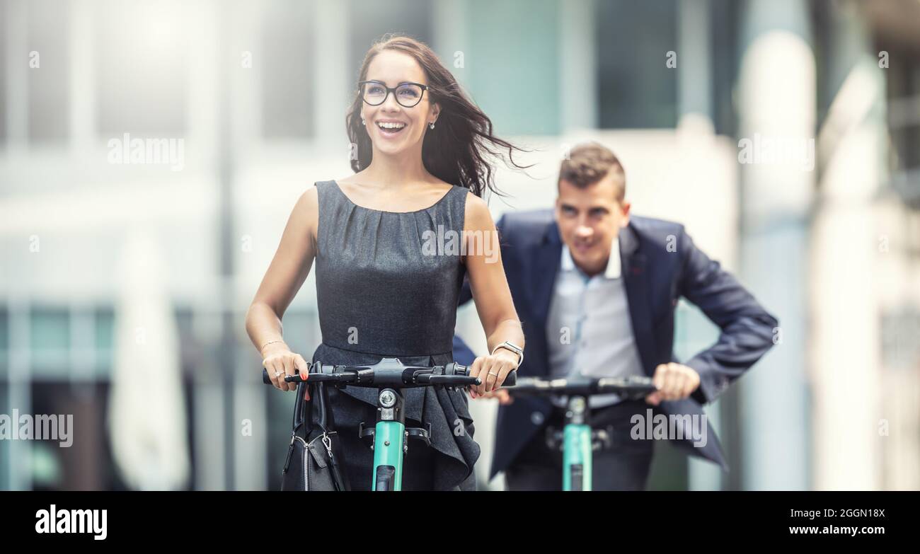 Two work colleagues having fun on electric scooters chasing one another in the city. Stock Photo
