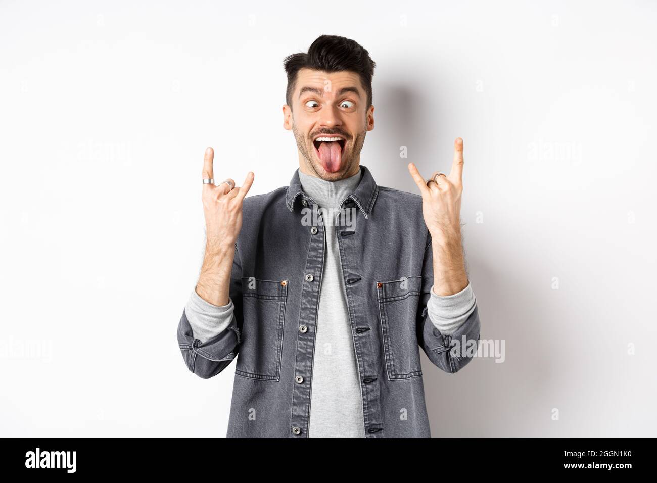 Squinting Rocks Funny young man showing tongue and rock horns, squinting eyes to fool ...