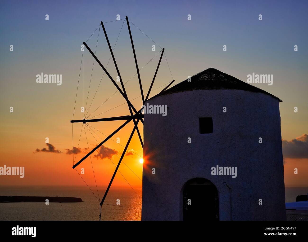 Landscape view of the setting sun over the Aegean Sea behind a traditional windmill Oia, Santorini, a Mediterranean Greek Island in the Cyclades group Stock Photo