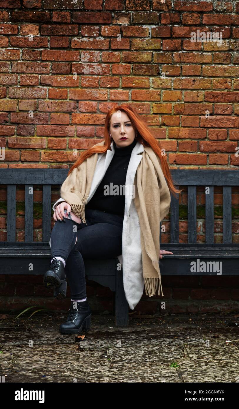 Woman with long red hair sitting on a bench in front of an old brick ...