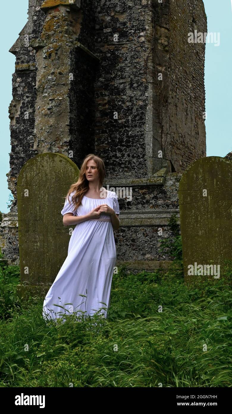young woman in plain white dress looking melancholy at the ruins of an old church. (book cover style) Stock Photo