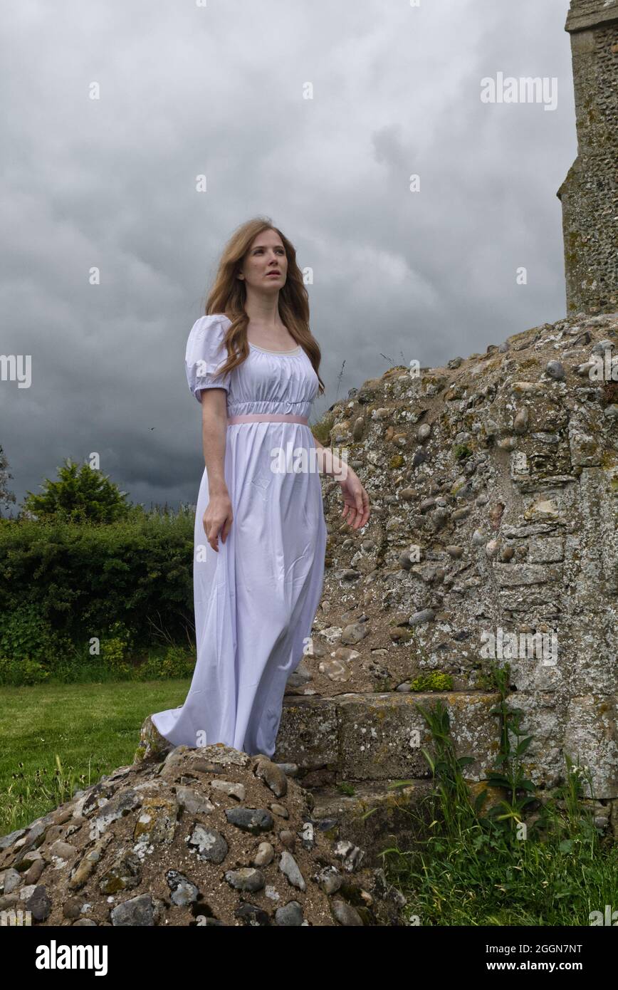 young woman in plain white dress looking melancholy at the ruins of an old church. (book cover style) Stock Photo