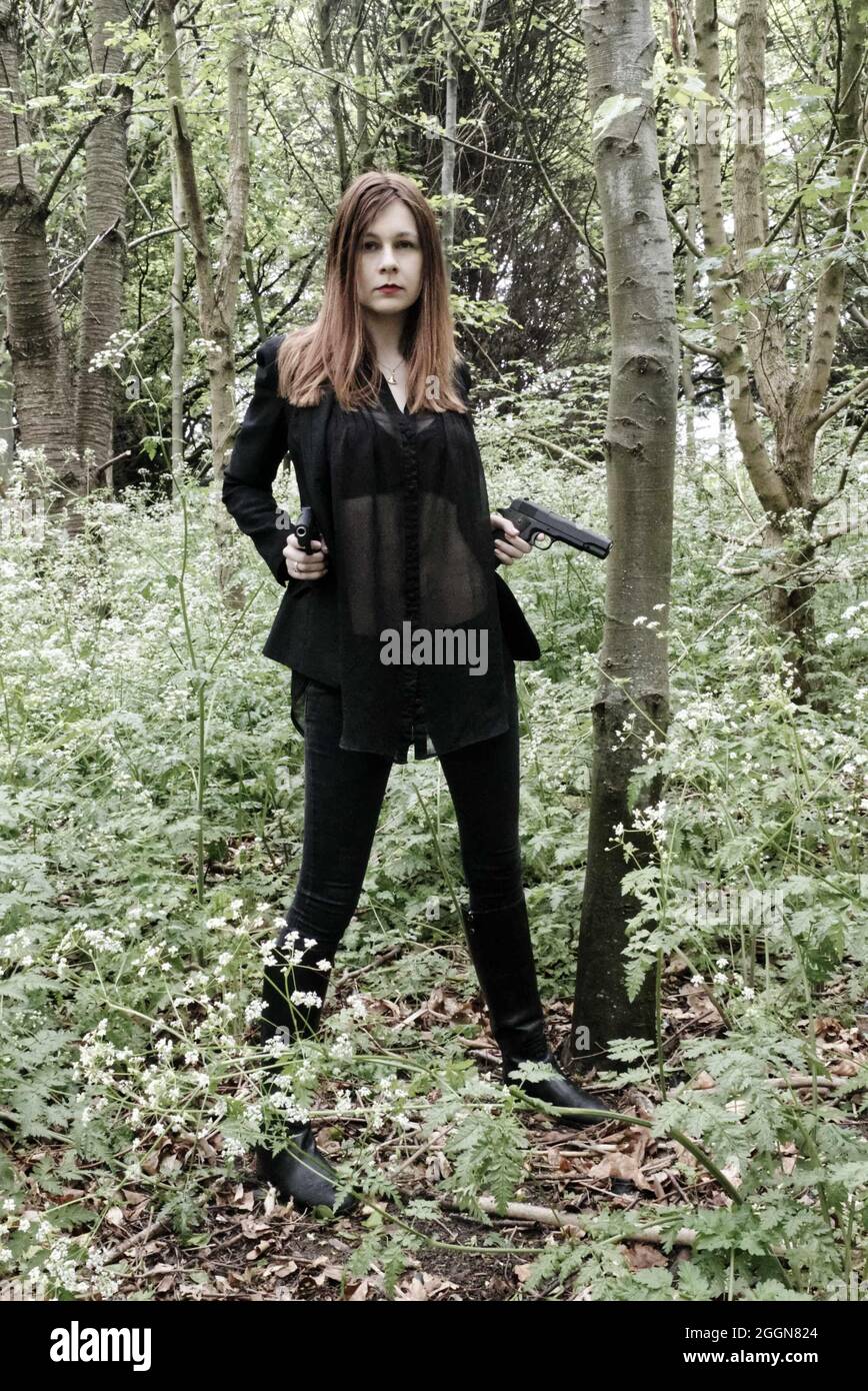 gun toting young woman in the woods dressed in black, female secret agent style. Stock Photo