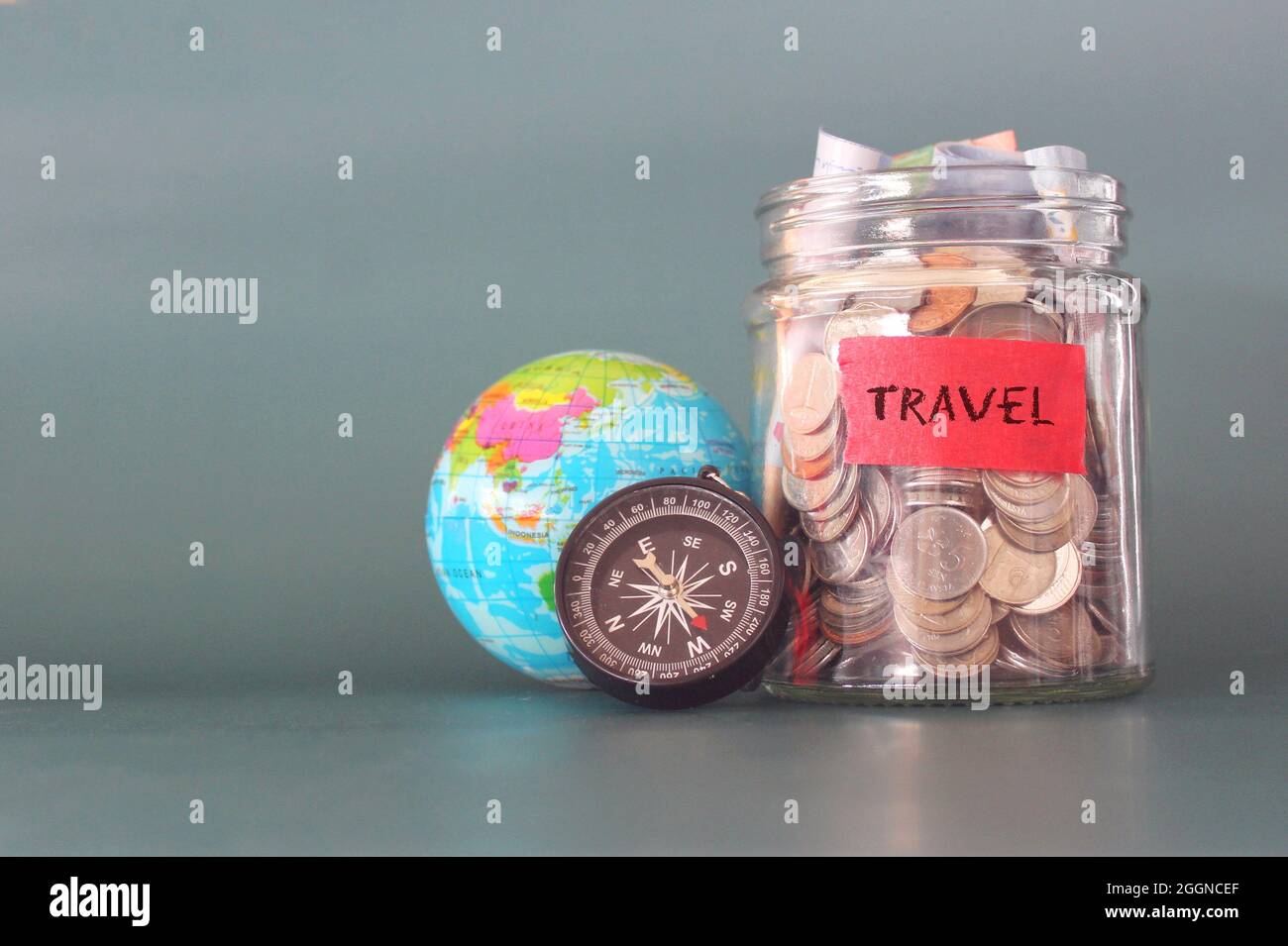 Travel budget concept. Coins in a glass jar, earth globe and compass with copy space for text. Stock Photo