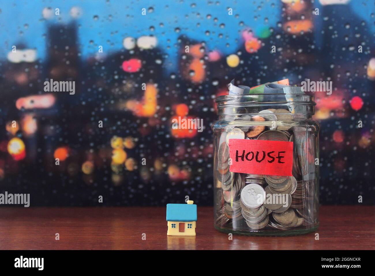 Real estate, property investment, saving money for house concept. Glass jar full of coins and miniature house with copy space for text Stock Photo