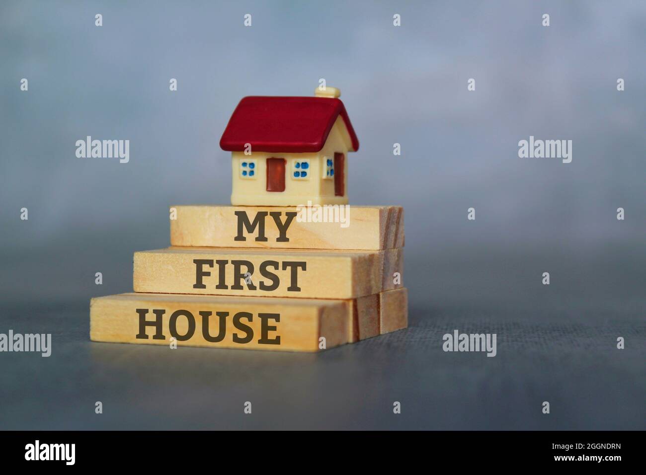Miniature house on top of wooden tiles with text MY FIRST HOUSE Stock Photo