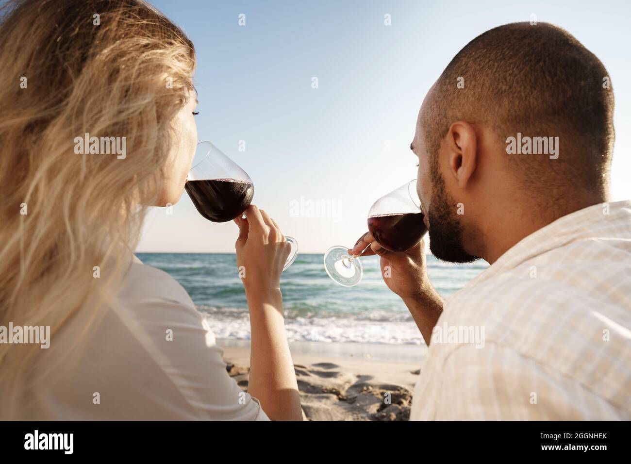 Portrait of a young couple sitting on the beach and drinking wine Stock ...