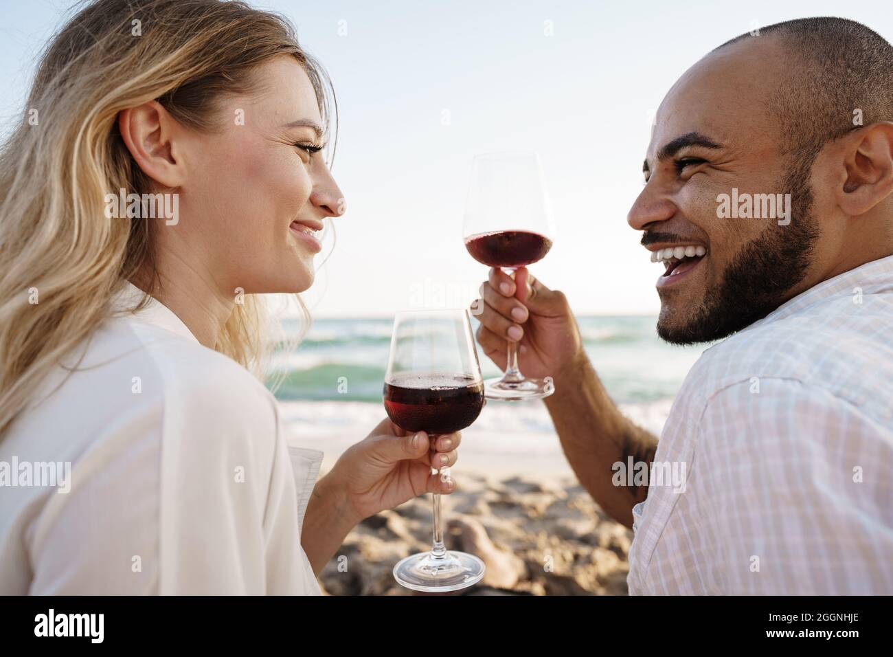 Portrait of a young couple sitting on the beach and drinking wine Stock ...