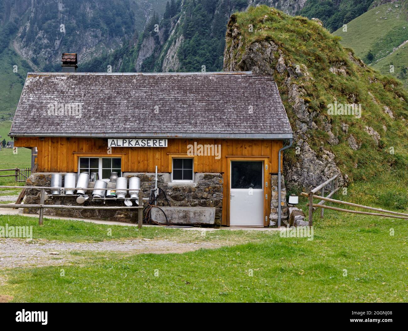 swiss alpine cheese dairy farm built in old style next to a rock wall empty milk cans in front of the house, german alp cheese dairy sign, text transl Stock Photo