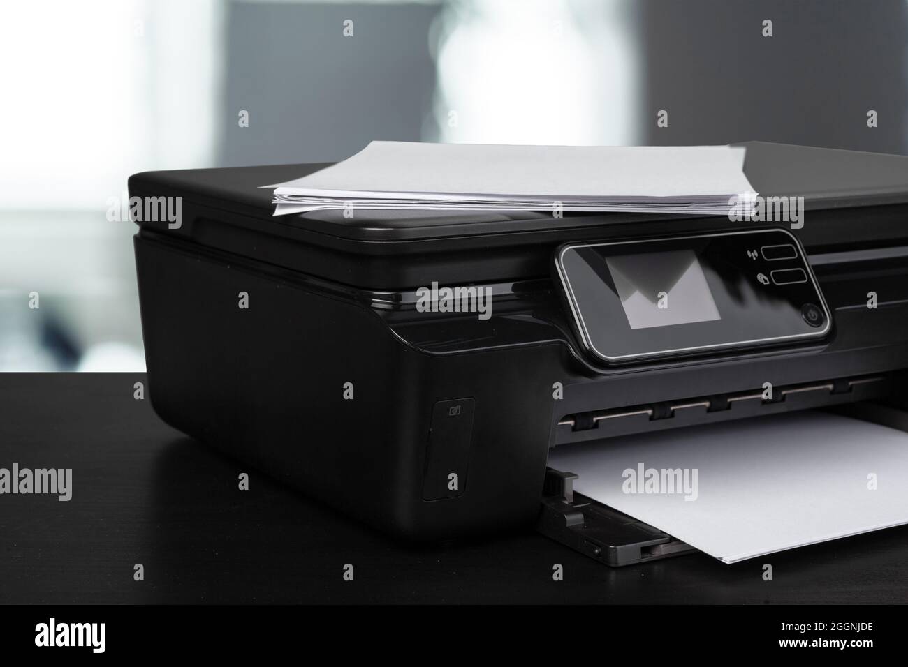 Compact laser printer on black desk against blurred background Stock Photo