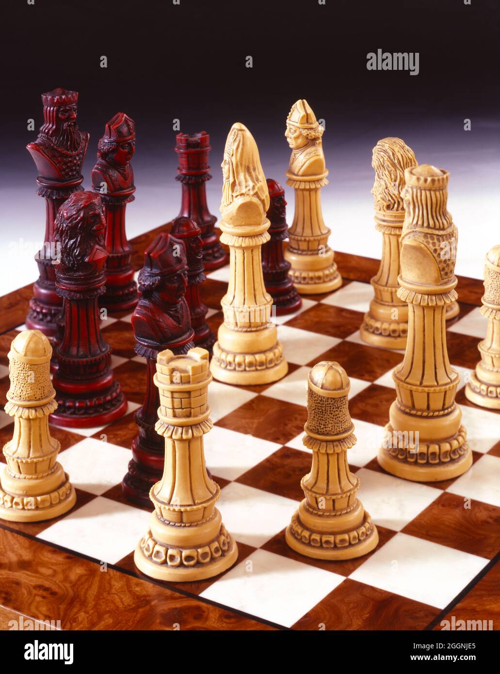carved chess pieces on wooden board graduated grey background copy space Stock Photo