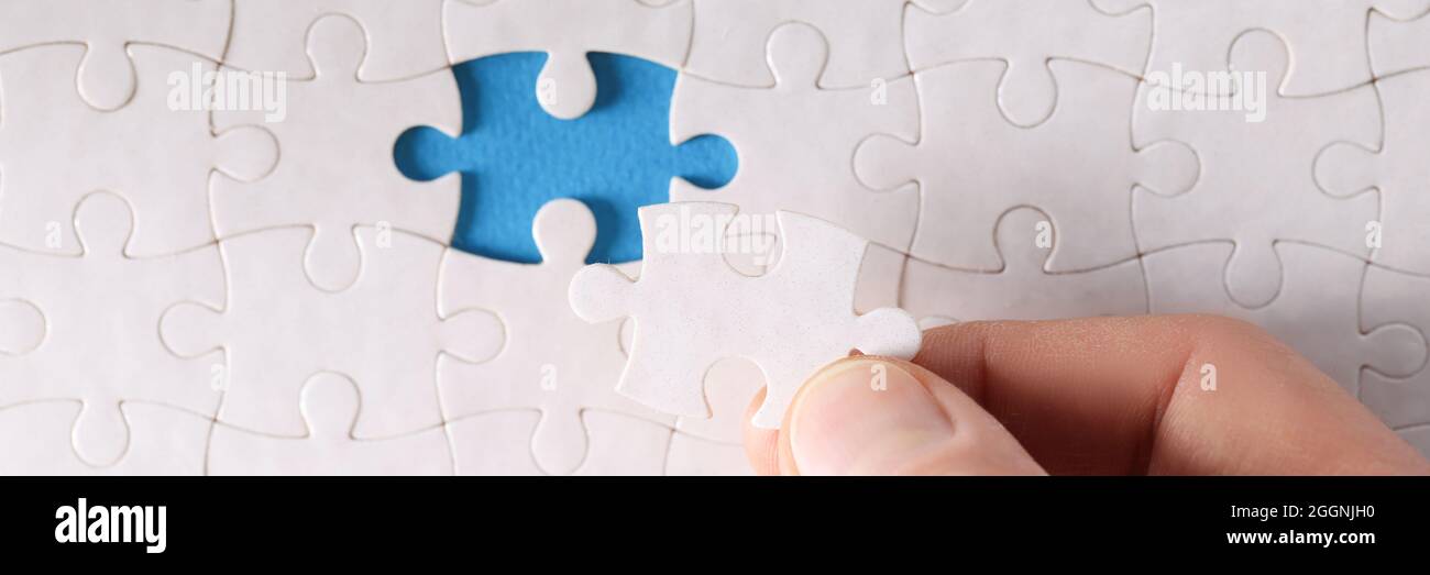 Man inserting last piece into white puzzle closeup Stock Photo