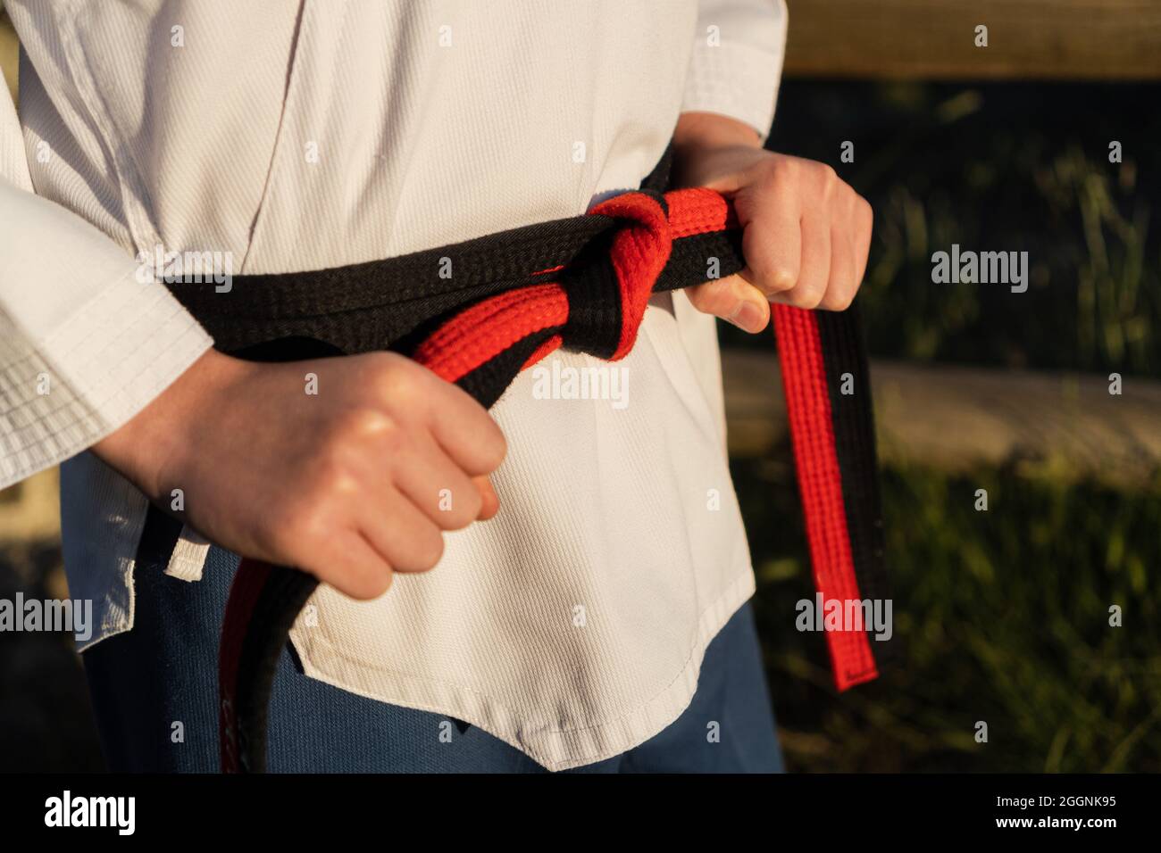 Young karate boy attaching on a black belt on his taekwondo uniform before training outdoors. Sport, discipline and martial arts concept. Stock Photo