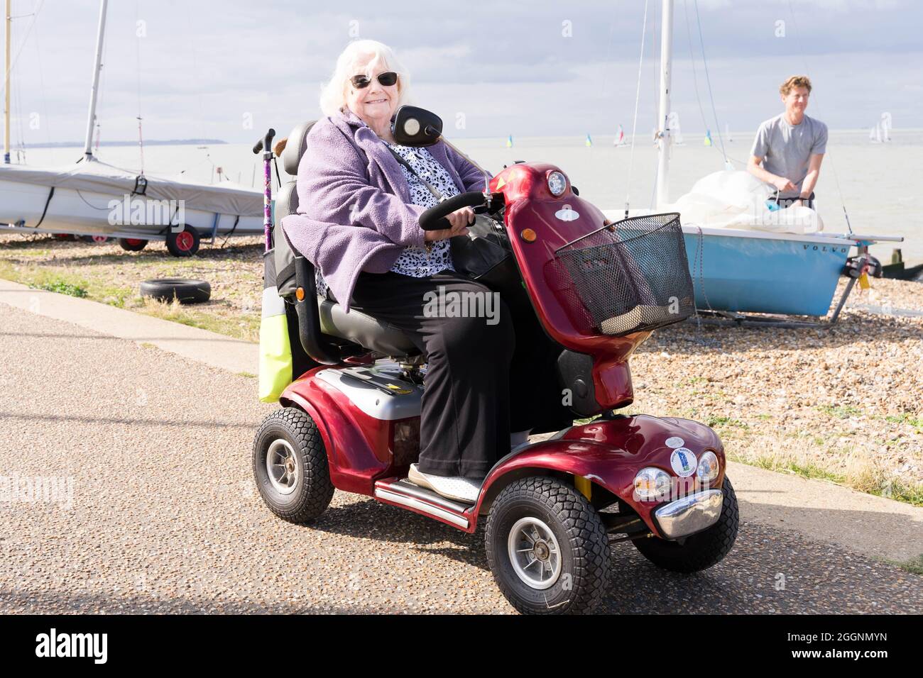 woman in mobility wheelchair / bike enjoys sunny day out at beach side town, watching sailing race at Tankerton Kent England Stock Photo