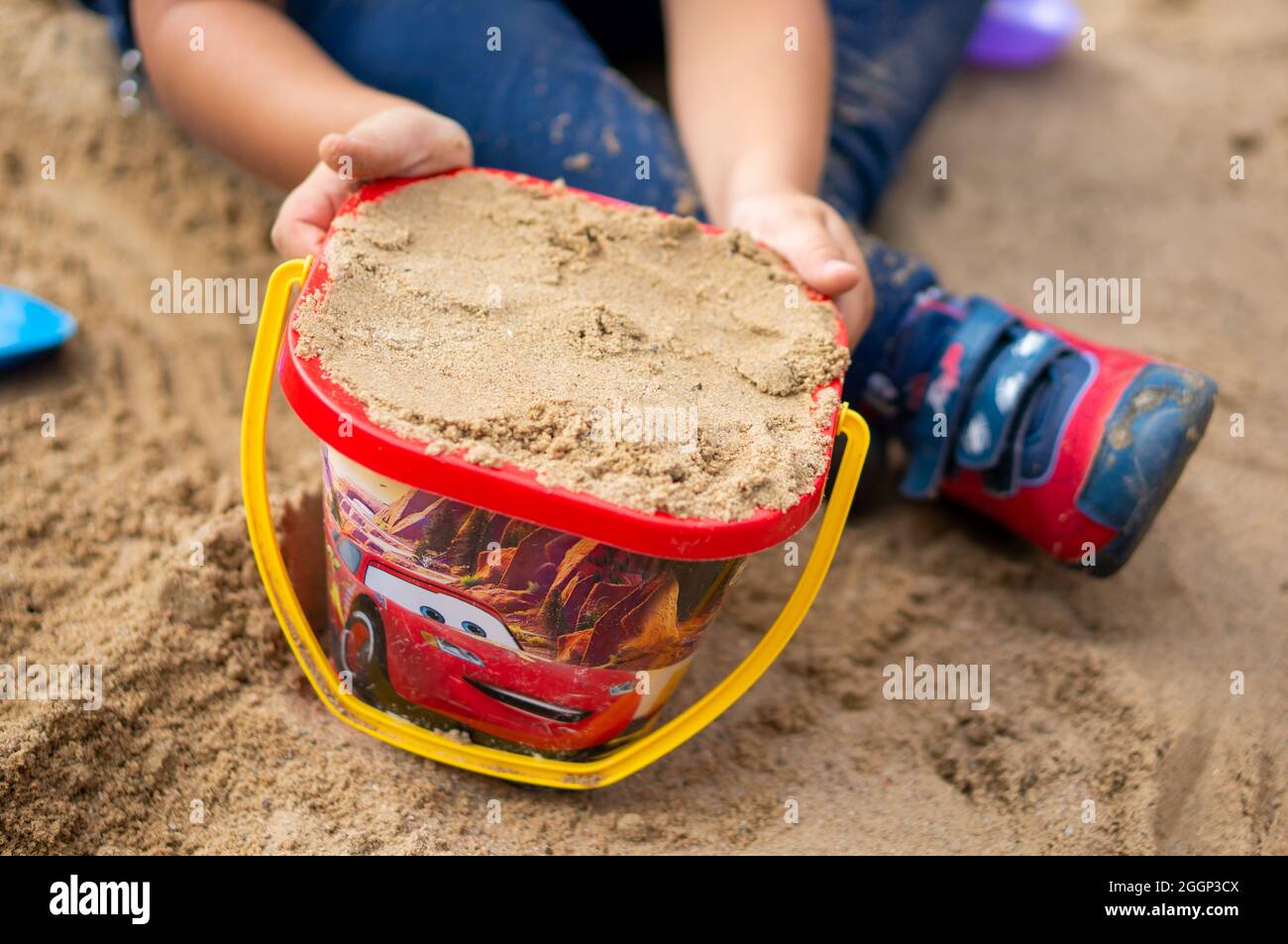 POZNAN, POLAND - Aug 25, 2018: A child playing with a plastic red toy bucket with Disney Cars cartoon character Lighting Mcqueen Stock Photo