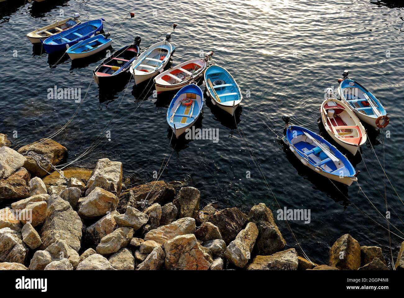 Drone shot of a colored boats aligned by rocks in the sunny water sea ...