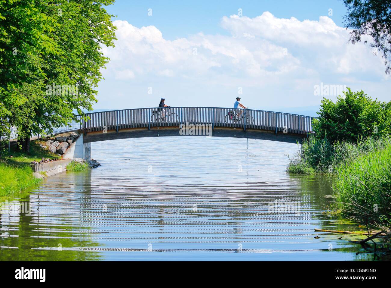 Zwei Fahrradfahrer überqueren die Brücke über den Bach Aach bei der Mündung in den Bodensee, Arbon im Thurgau, Schweiz Stock Photo