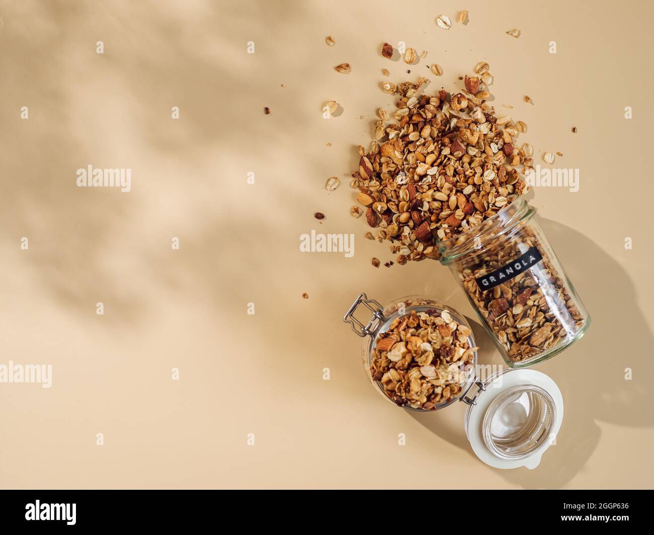 Homemade granola sprinkled of glass jar over pastel beige background