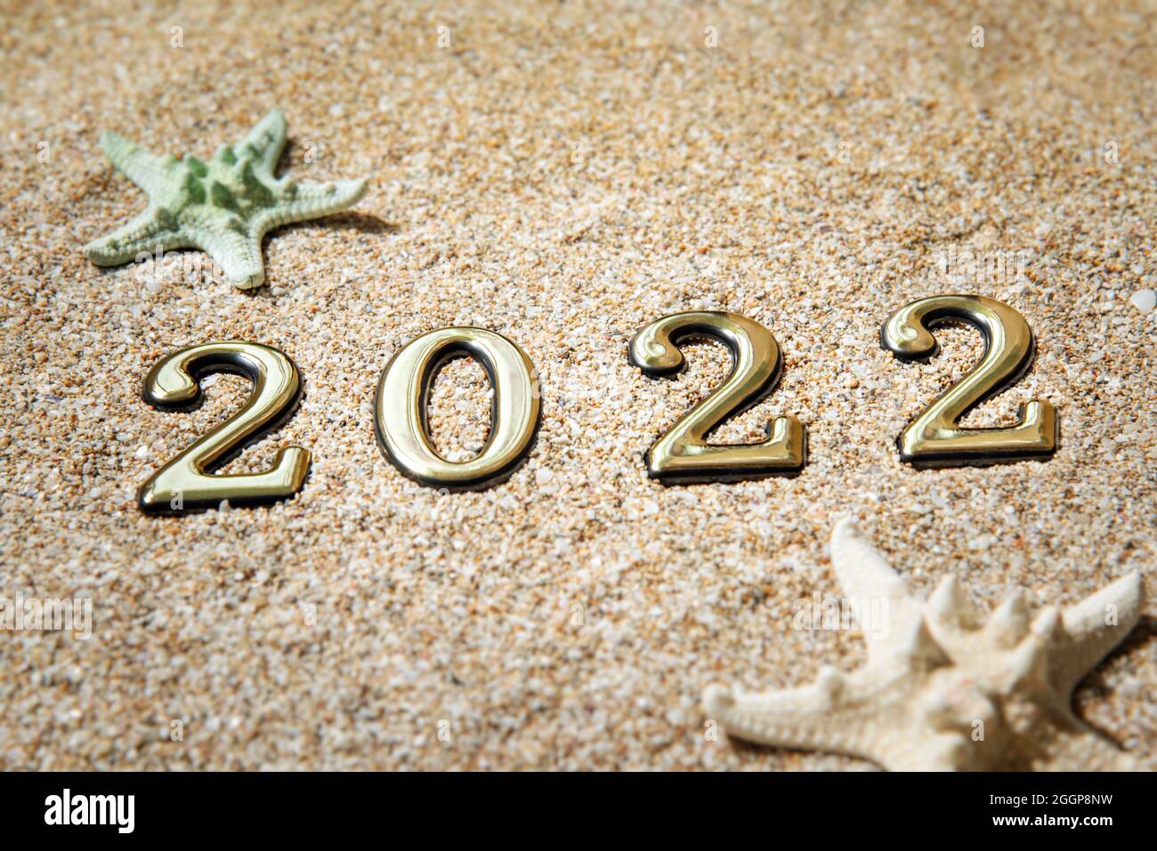 Beach season 2021 concept. Golden numbers 2022 and starfish on the sand by the sea. Stock Photo