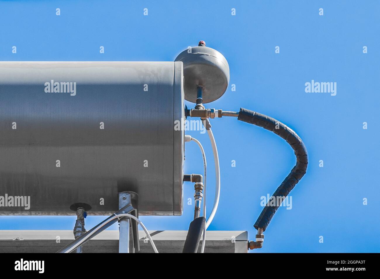 Water boiler heater tank system and hot technology on the roof of the house against the blue sky. Stock Photo