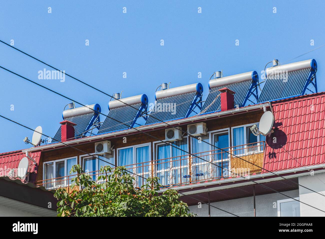 Thermal solar panels and water heater alternative technologies of water heating on the roof of the hotel against the blue sky outdoor. Stock Photo