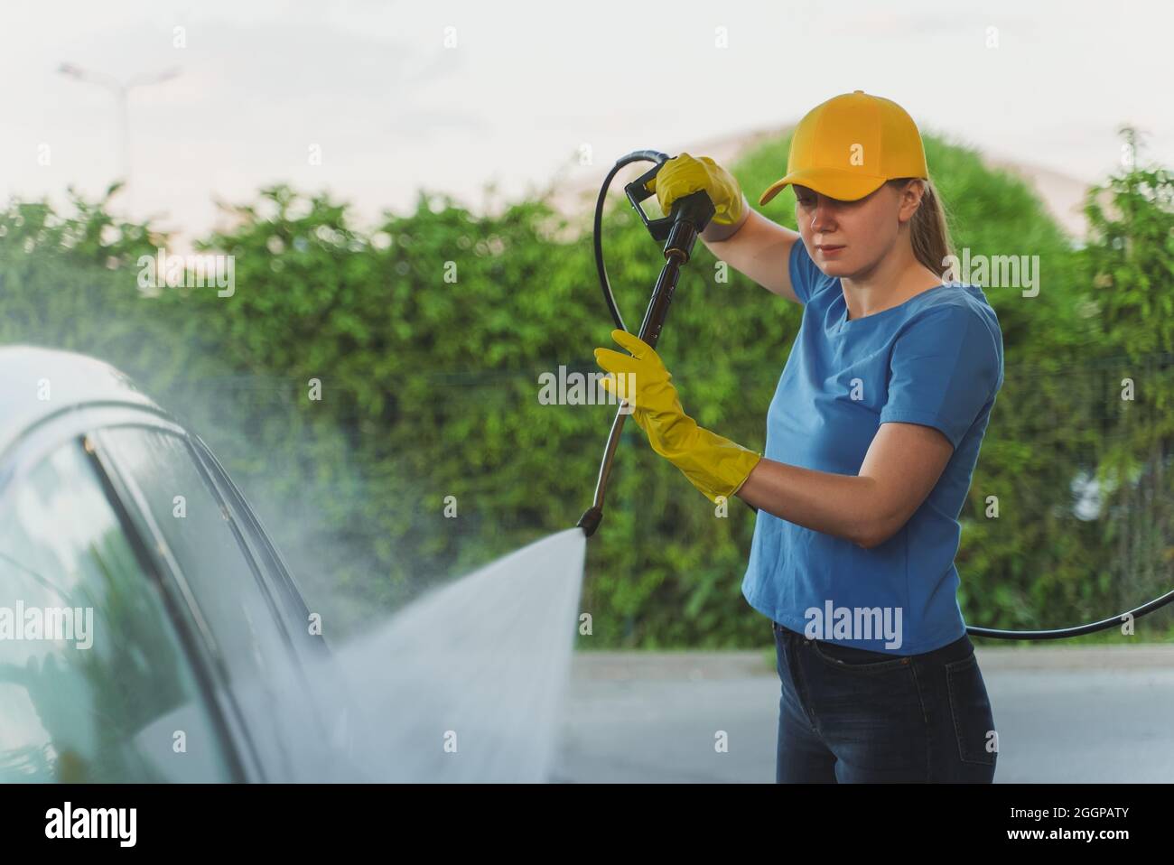 Woman in uniform cleaning car using high pressure water. Car wash