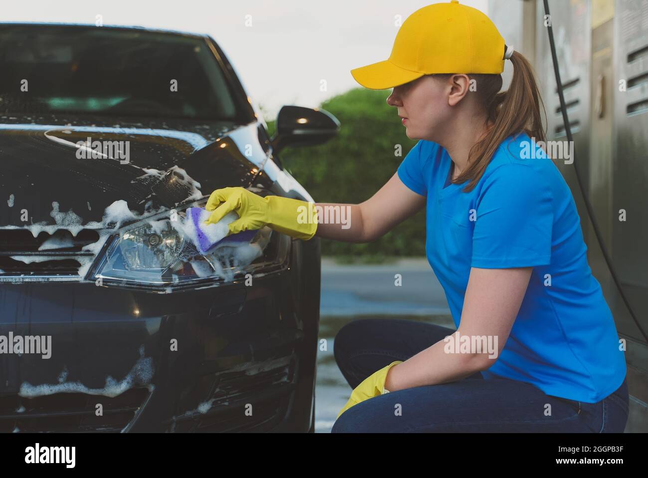 Woman in uniform cleaning car with sponge. Car wash service. Stock Photo