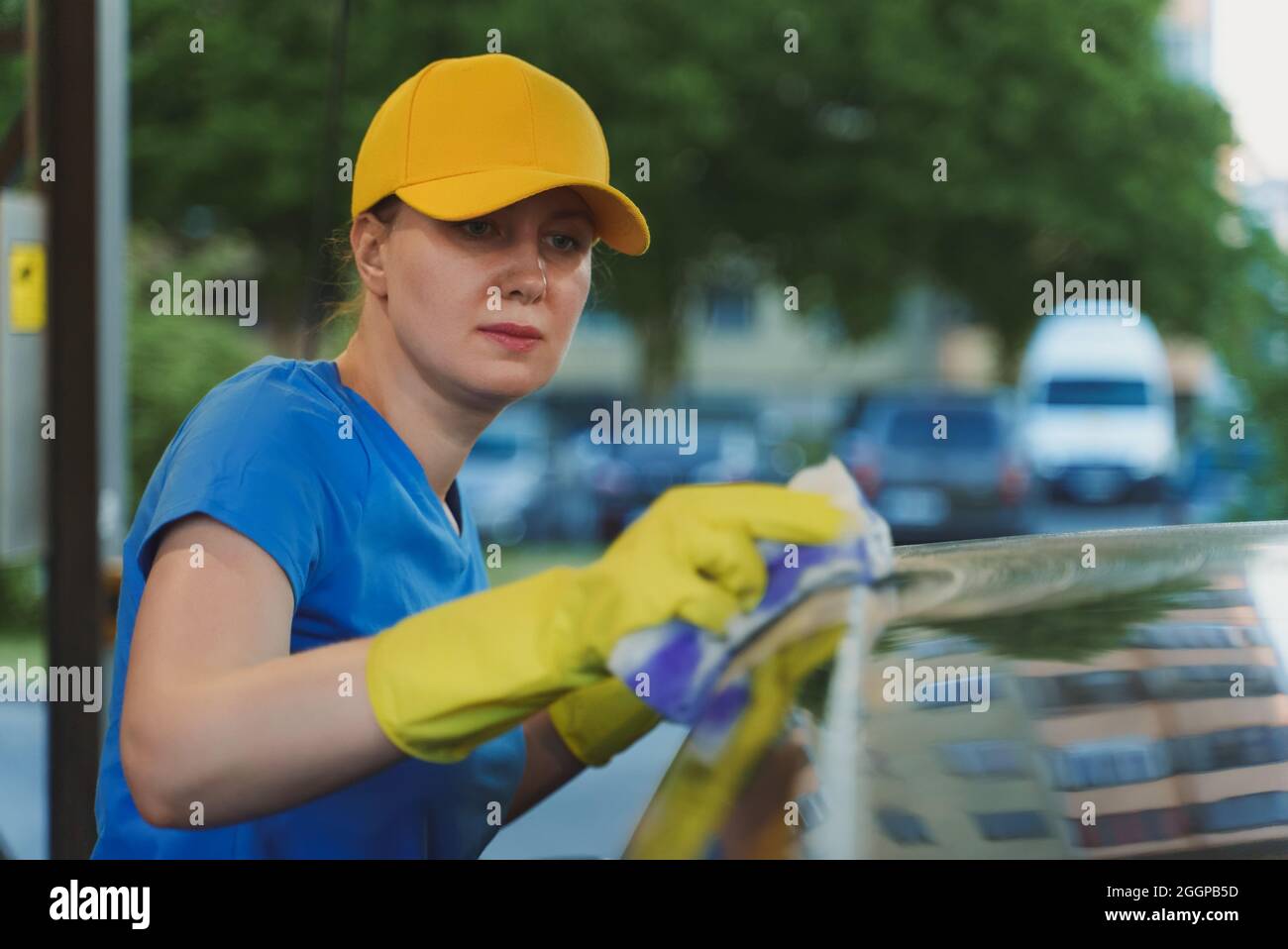 Woman in uniform cleaning car with sponge. Car wash service. Stock Photo