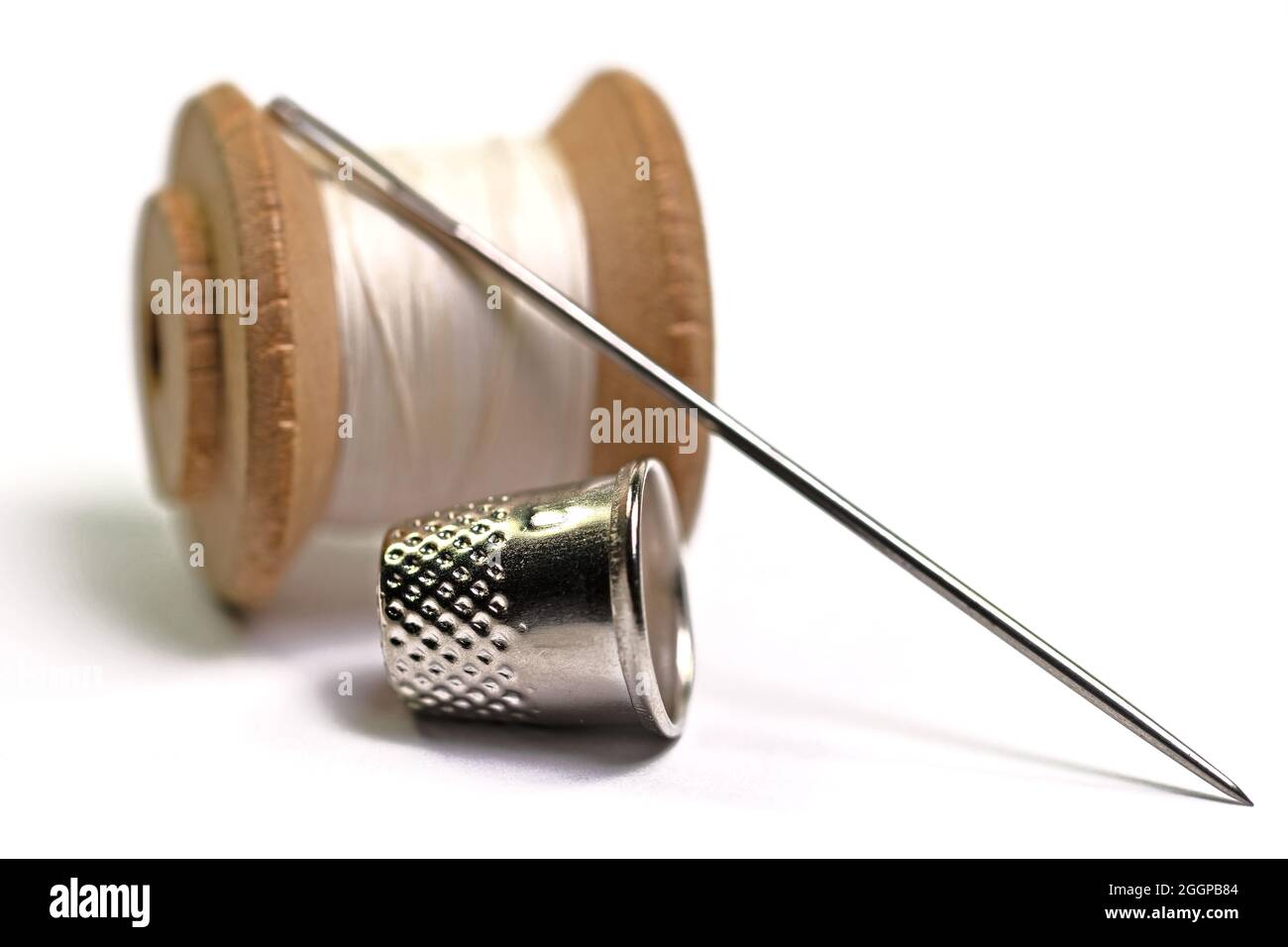 Thimble, sewing needle and thread against white background Stock Photo