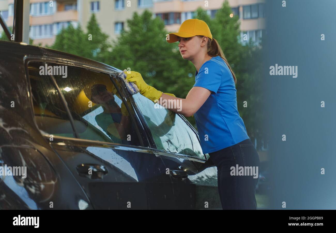 Woman in uniform cleaning car with sponge. Car wash service. Stock Photo