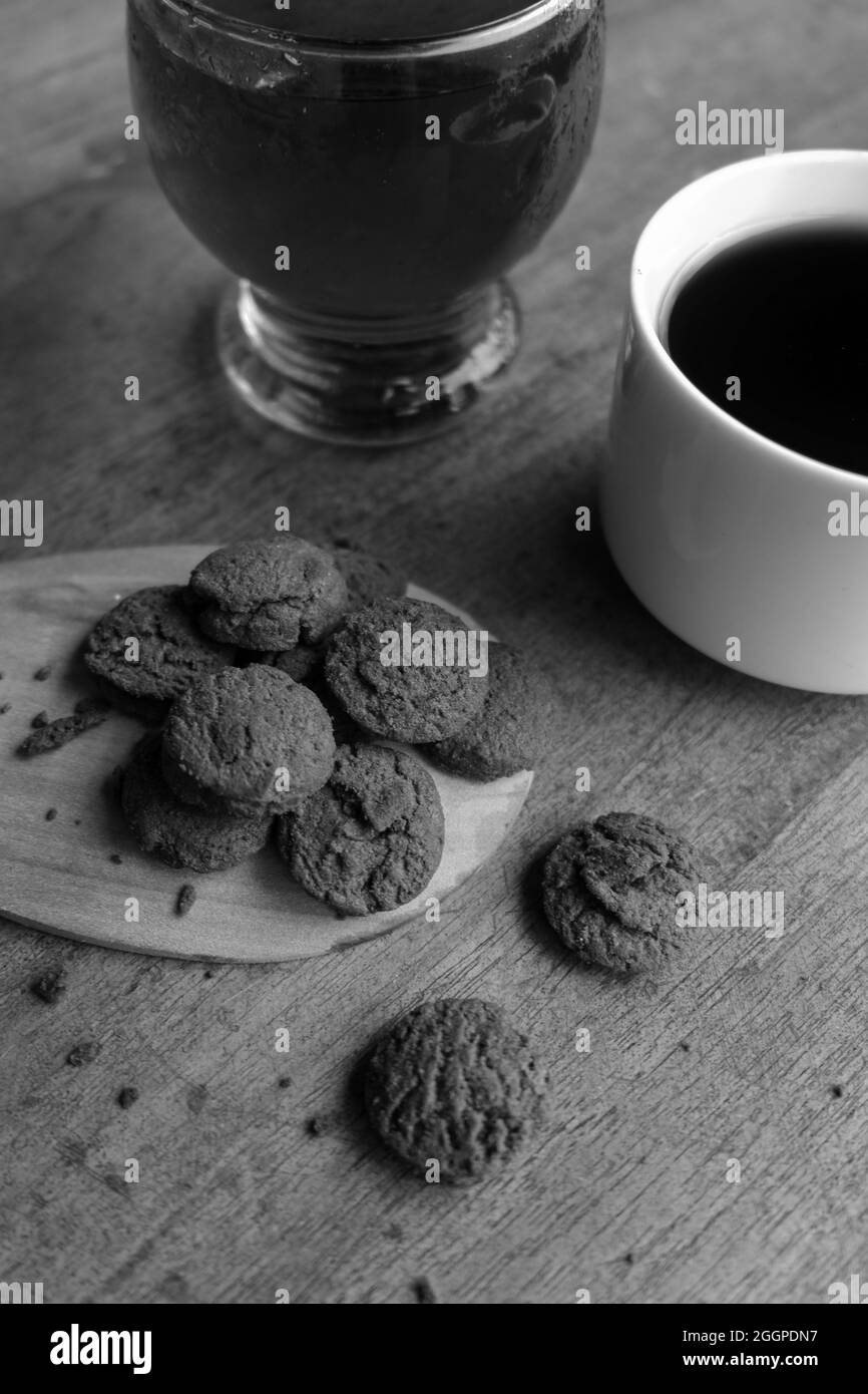 Grayscale shot of chocolate cookies, a cup of coffee, and a glass of juice on a wooden table Stock Photo