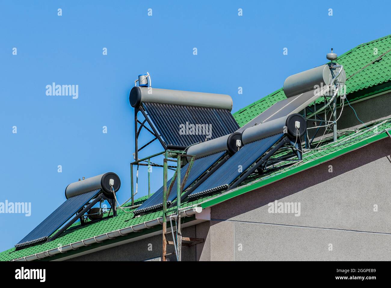 Thermal solar panels water heaters alternative technology of water heating on the roof tile of the house against the blue sky background. Stock Photo
