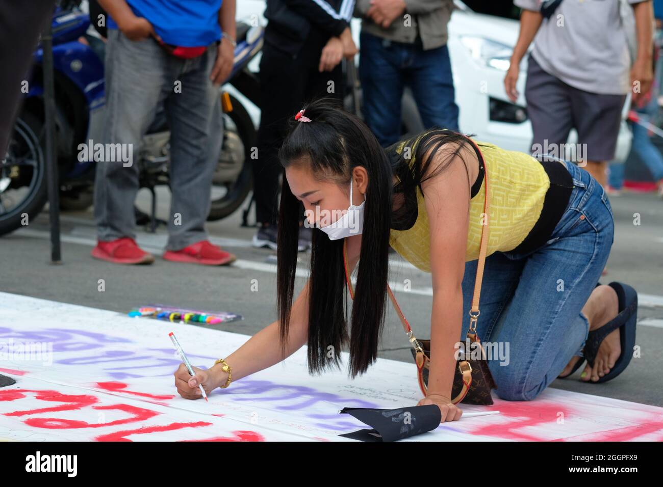 Bangkok, Thailand, 2 September 2021, a female protestor contributes to a protest banner demanding the resignation of Thailand's Prime Minister General Prayut Chan-ocha. The protest closed the north-south carriageways of the Asoke road junction in central Bangkok, and restricted traffic along the Sukhumvit Road. Today's event was part of an on-going series of protests across the country to voice disaffection with the current government's performance during the COVID pandemic. Stock Photo