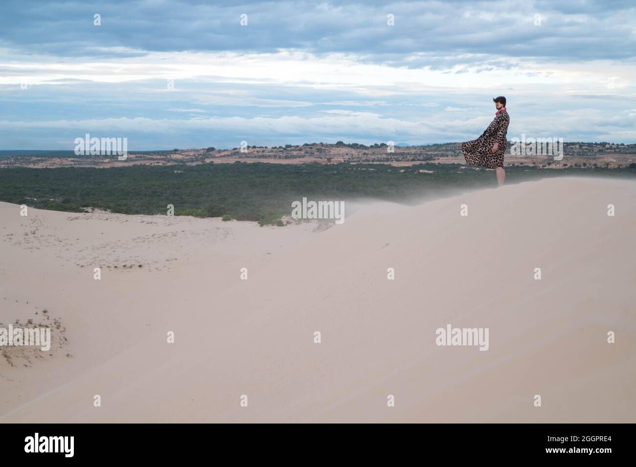 Wanderer walking in the desert. Young man standing in white sand dunes. Stranger in desert. Sand flies in the wind. Clothes fluttering in the wind Stock Photo
