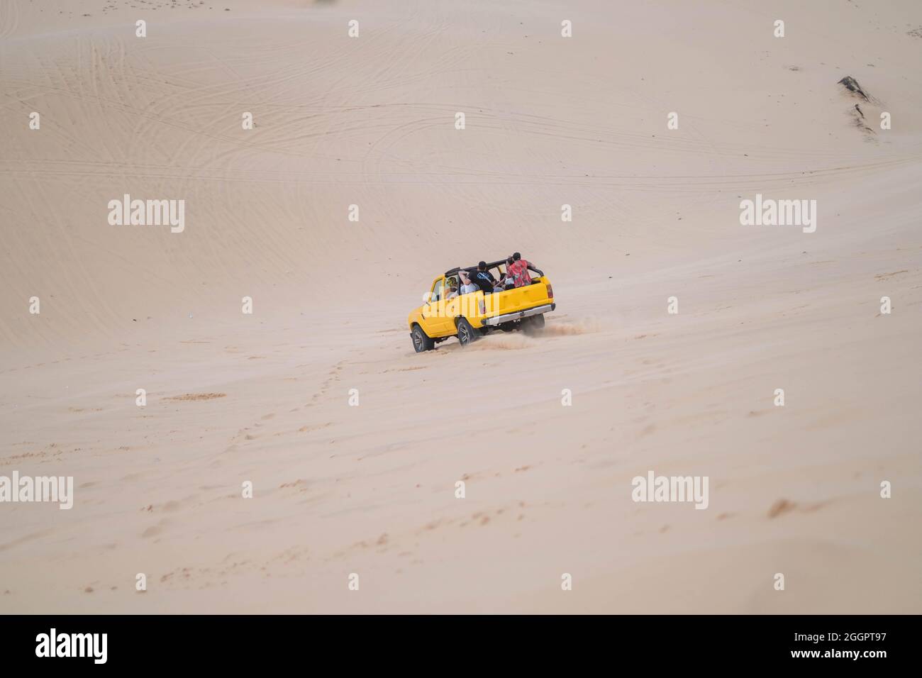Picturesque view of big car driving on sandy dunes and tire tracks on sand on sunny day during summer vacation. Sand dunes. Tourists in desert. Stock Photo