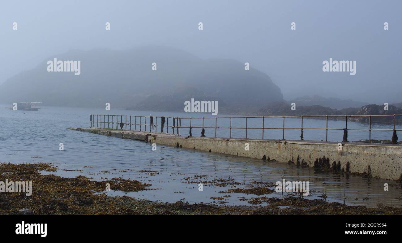 Looking into the mist over Tarbet bay, Scotland, to the walkway and handrail down to the landing area for the boat to Handa Island Stock Photo