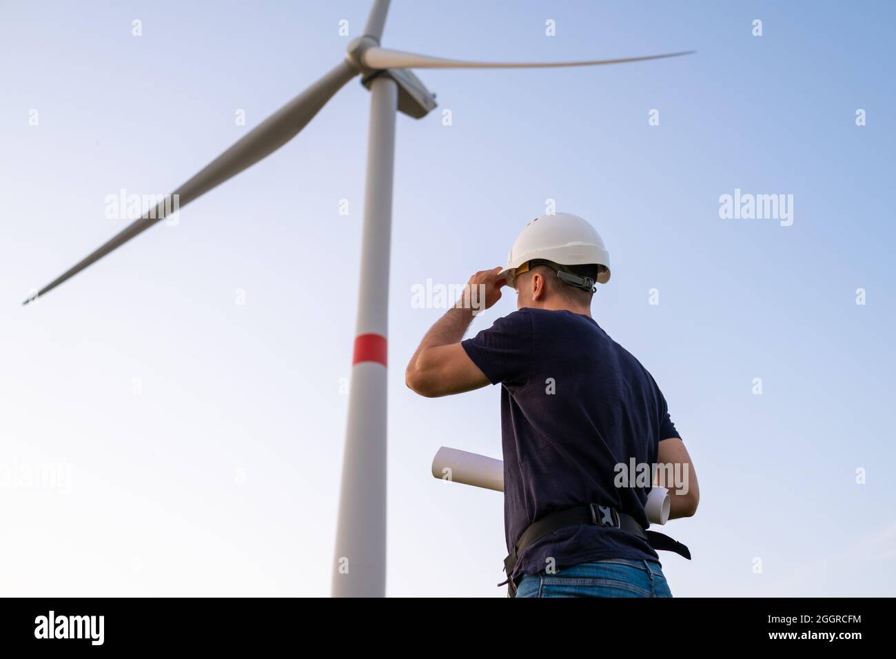 Engineer in hard hat holds a plan project for the construction of wind turbines in the field against the background of windmills. Generation of Stock Photo