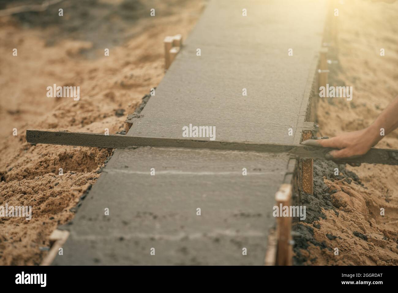 Worker leveling newly poured cement into formwork with reinforcement