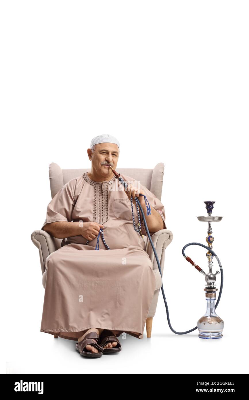 Mature man in ethnic clothes seated in an armchair smoking shisha isolated on white background Stock Photo