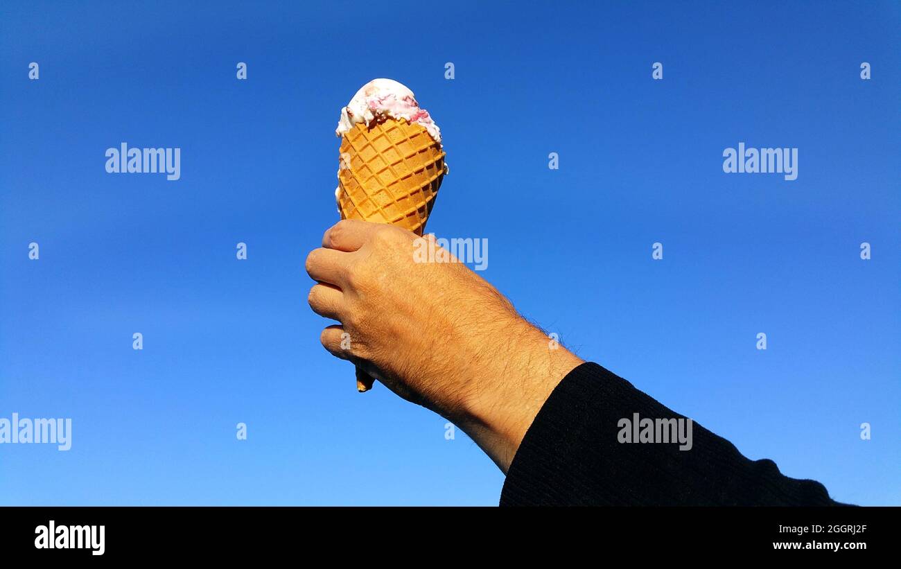 Isolated gelato ice cream cone in hand against blue sky, blue backdrop Stock Photo