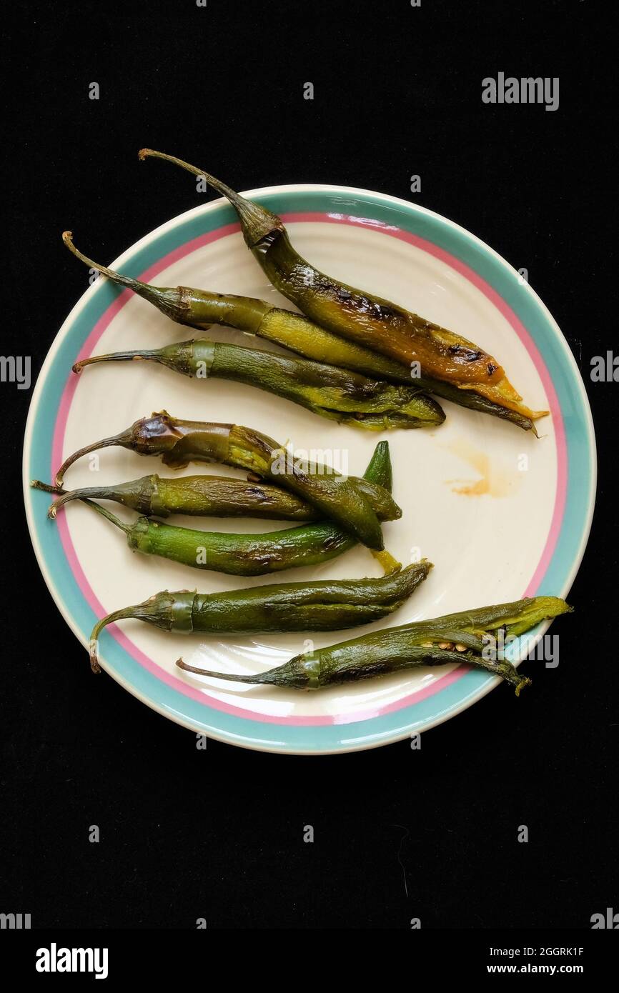 Roasted and peeled serrano peppers with stems on a ceramic plate, ready for homemade salsa and an ingredient for spicy Mexican food. Stock Photo