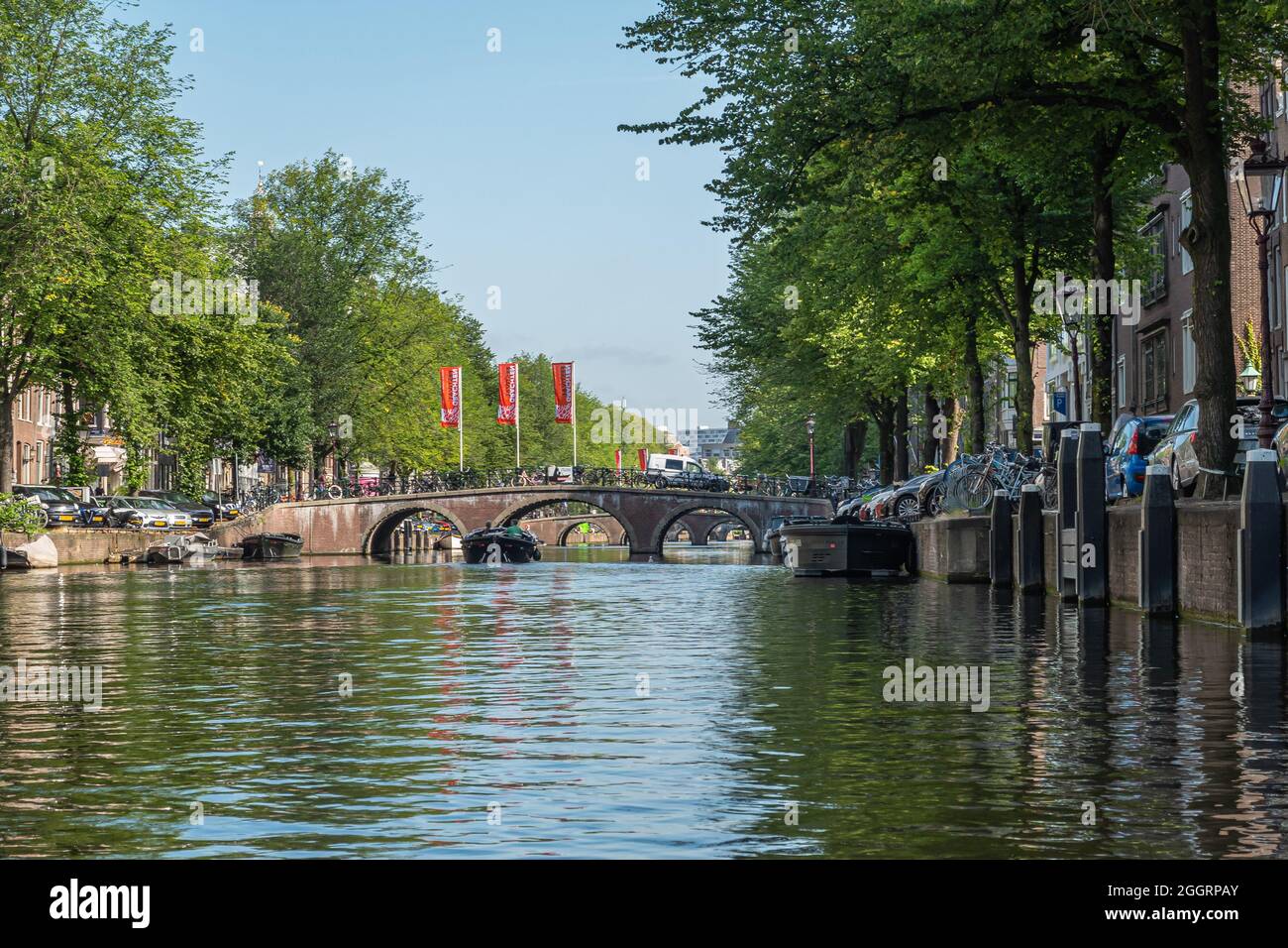 Amsterdam, Netherlands August 15, 2021: Stone bridge with 3 arches over wider canal green foliage and parked cars on both shores under blue sky Stock Photo - Alamy