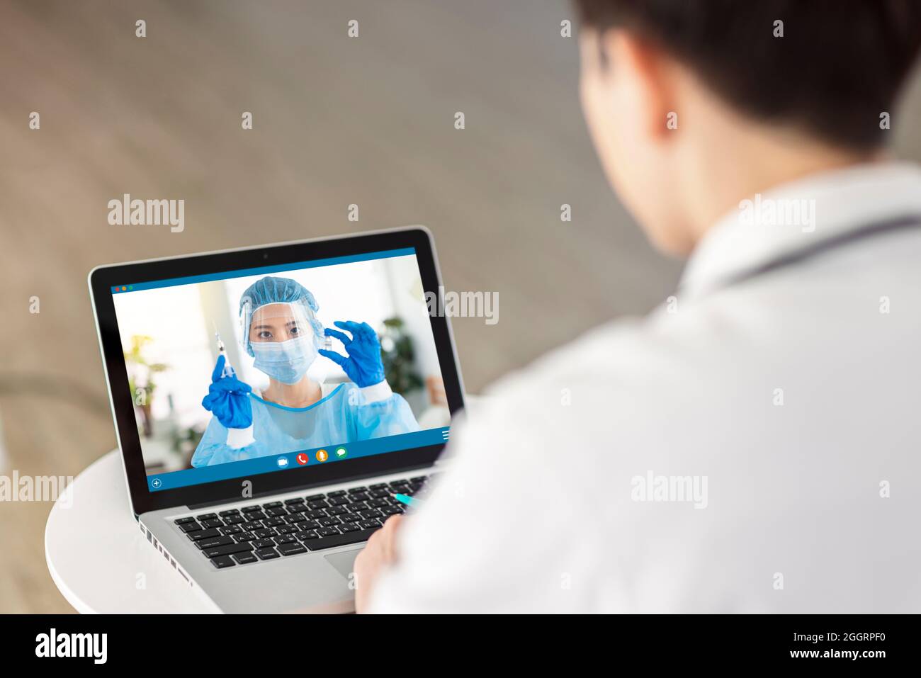 Back view of doctor making video call with his colleague.Healthcare worker with syringe in video. Stock Photo