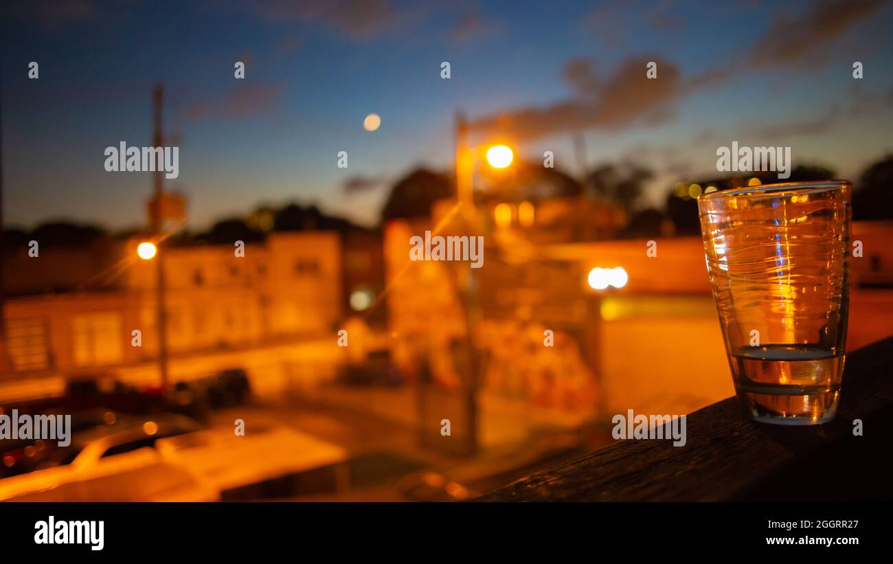 Orange city lights, windows, streets under blue and crimson sunset sky with crescent moon Stock
