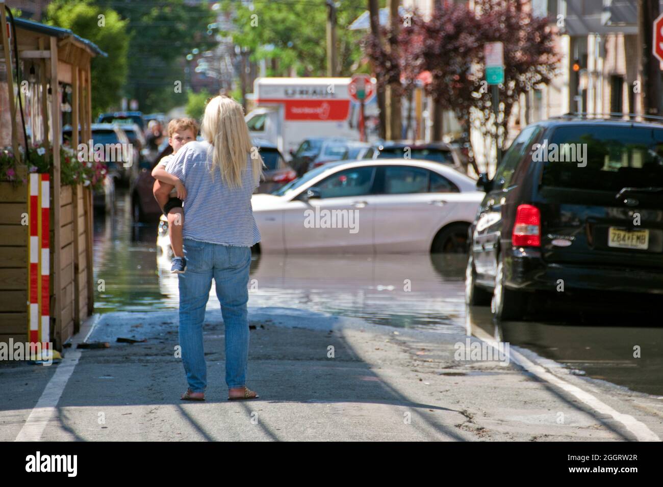 A woman with child looks at flooded cars on a street in Hoboken, New Jersey, caused by Hurricane Ida rain, Sept. 1 2021. Stock Photo