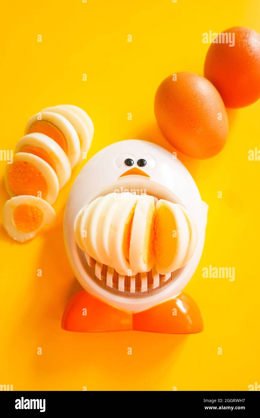 Funny egg slicer with hard boiled eggs whole ,  peeled and sliced on a yellow background Stock Photo