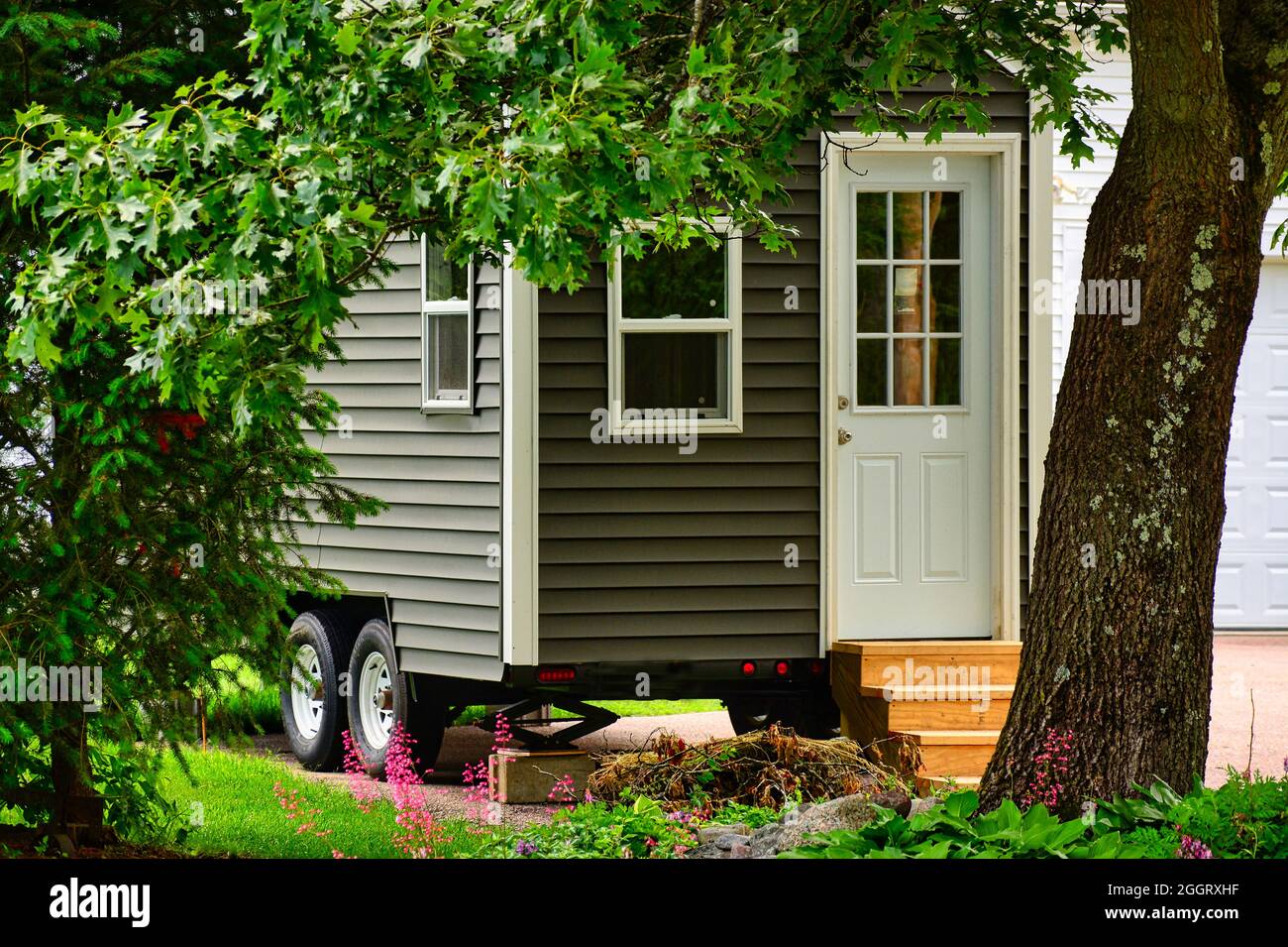 Tiny home on wheels framed by trees and flowers Stock Photo
